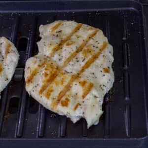 One cooked chicken breast on the grill plate on a George Foreman grill.