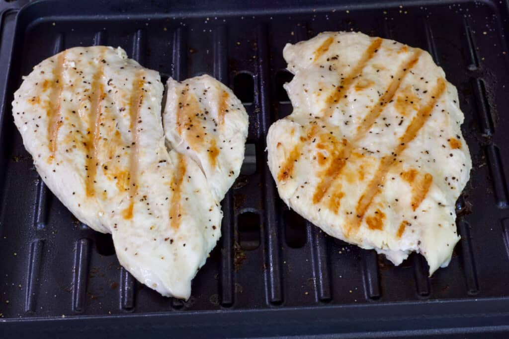Two cooked boneless chicken breasts on the grill plate of a George Foreman grill.