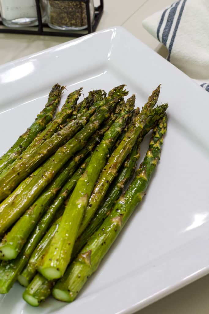 One pound of oven roasted asparagus spears on a white serving dish.