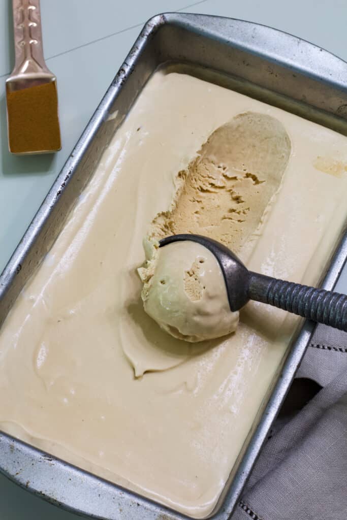 A loaf pan full of coffee ice cream, there is a scoop of ice cream in an ice cream scoop sitting on the pan.