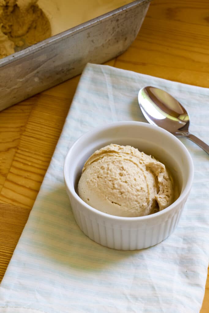A small white bowl with one scoop of coffee ice cream in it sitting on a blue and white striped napkin.