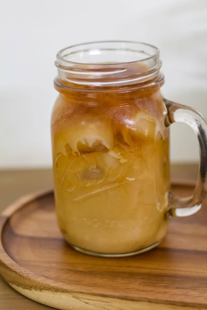 A Ball mason jar mug with iced cold brew coffee and milk in it.